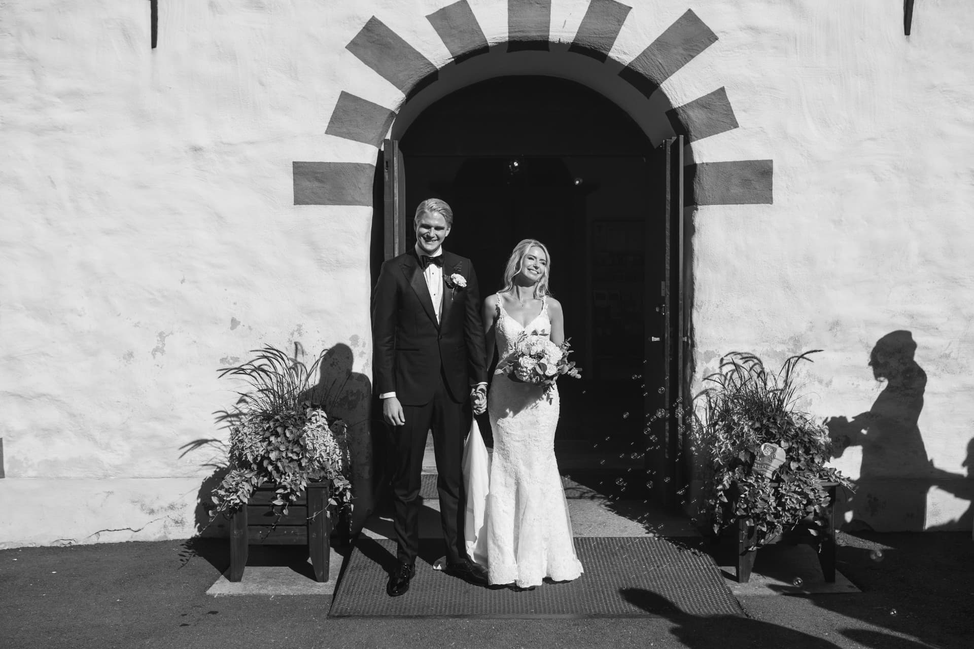 Brudparet står hand i hand i kyrkportalen efter vigseln, svartvitt – bröllopsfoto av Mehmet Budak