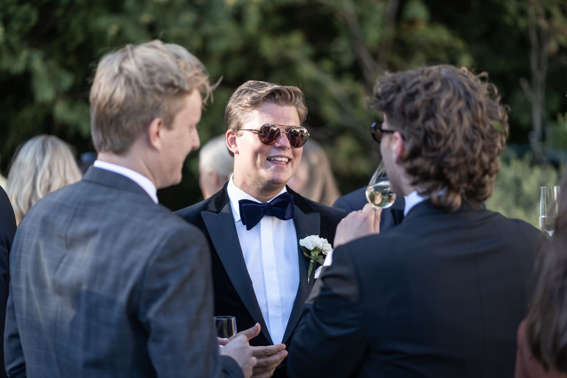 Gäster i smoking skrattar tillsammans under mottagningen – bröllopsfoto av Mehmet Budak