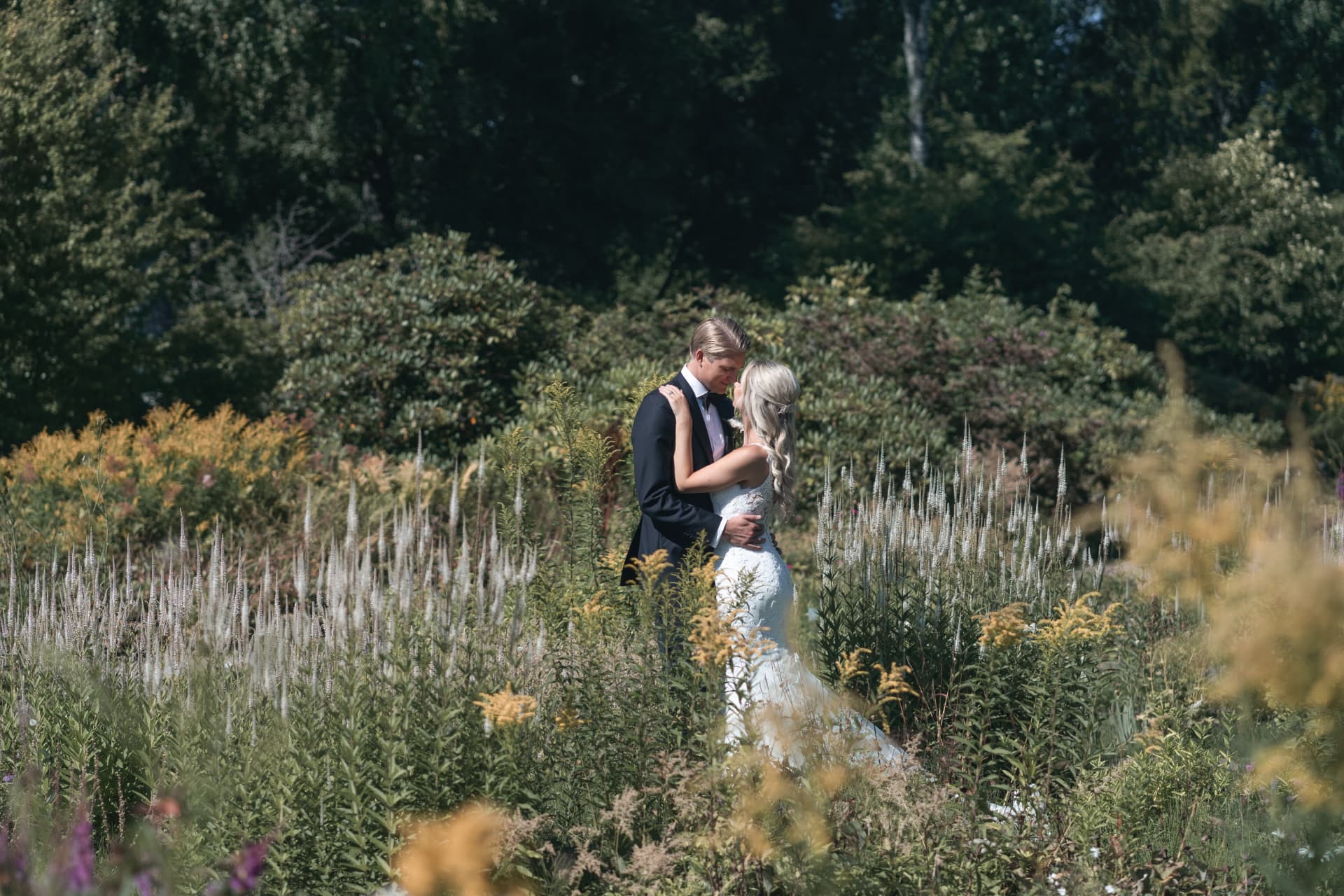Brudparet omfamnar varandra mitt i den blommande parken i Sunne – bröllopsfoto av Mehmet Budak