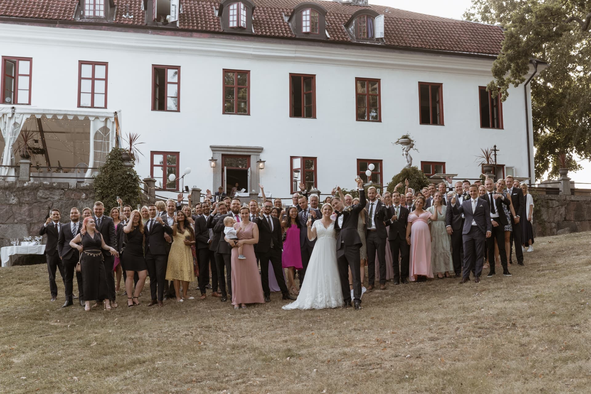 Alla gäster skålar tillsammans med brudparet framför herrgården – bröllopsfoto av Mehmet Budak