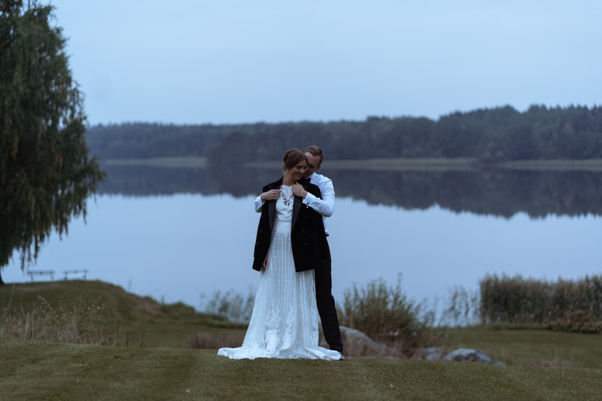 Anni & Emil – Brudgummen lägger kavajen om bruden vid Mälaren i skymningen