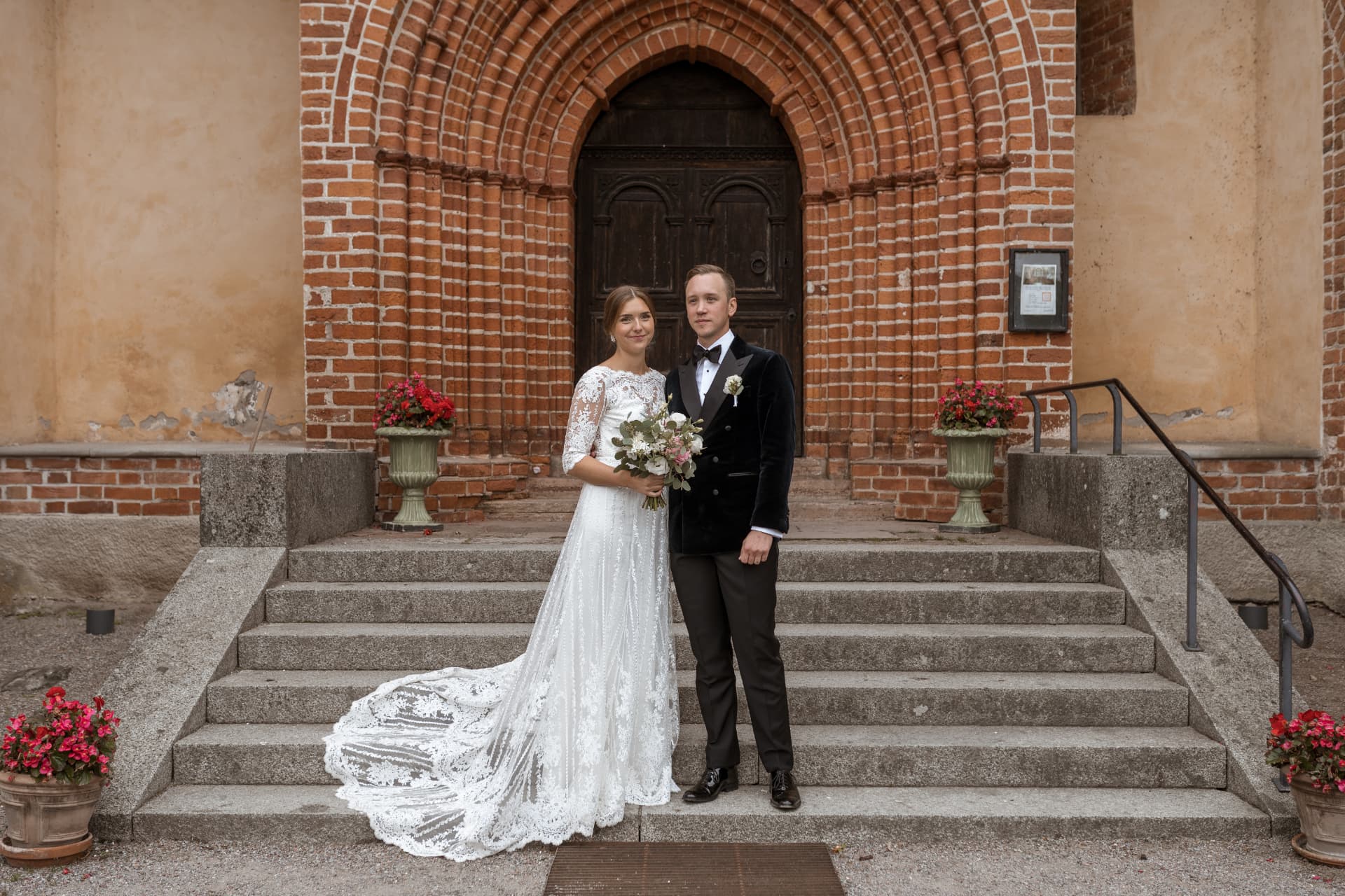 Brudparet framför kyrkans tegelportal efter vigseln – bröllopsfoto av Mehmet Budak