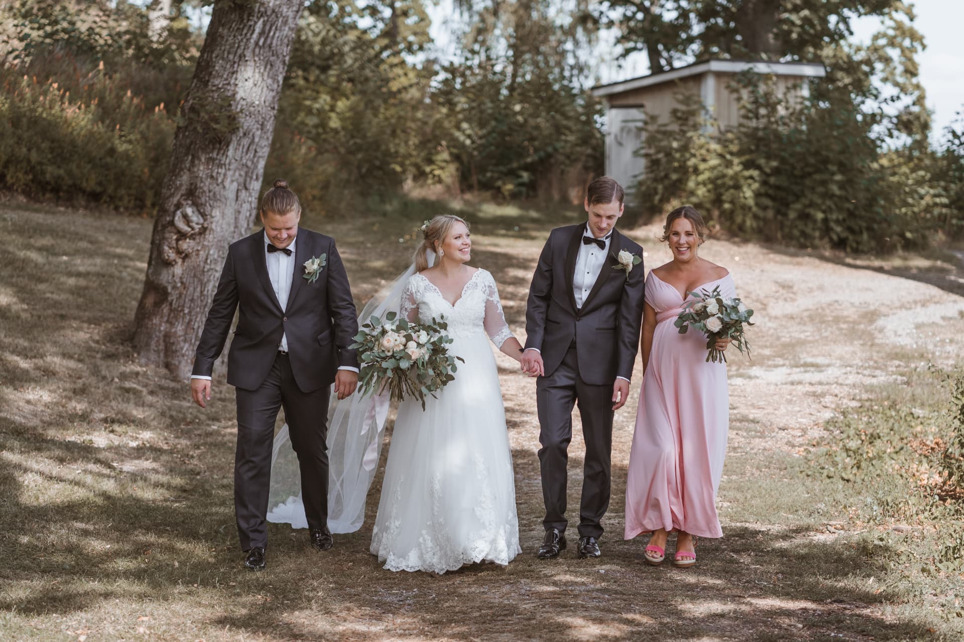 Brudparet går tillsammans med best man och brudtärna längs grusvägen – bröllopsfoto av Mehmet Budak