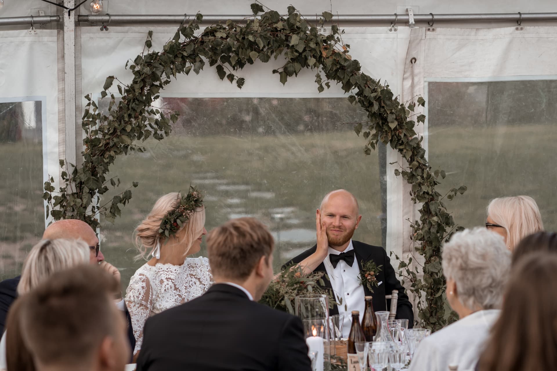 Bruden klappar brudgummen på kinden vid bordet – bröllopsfoto av Mehmet Budak