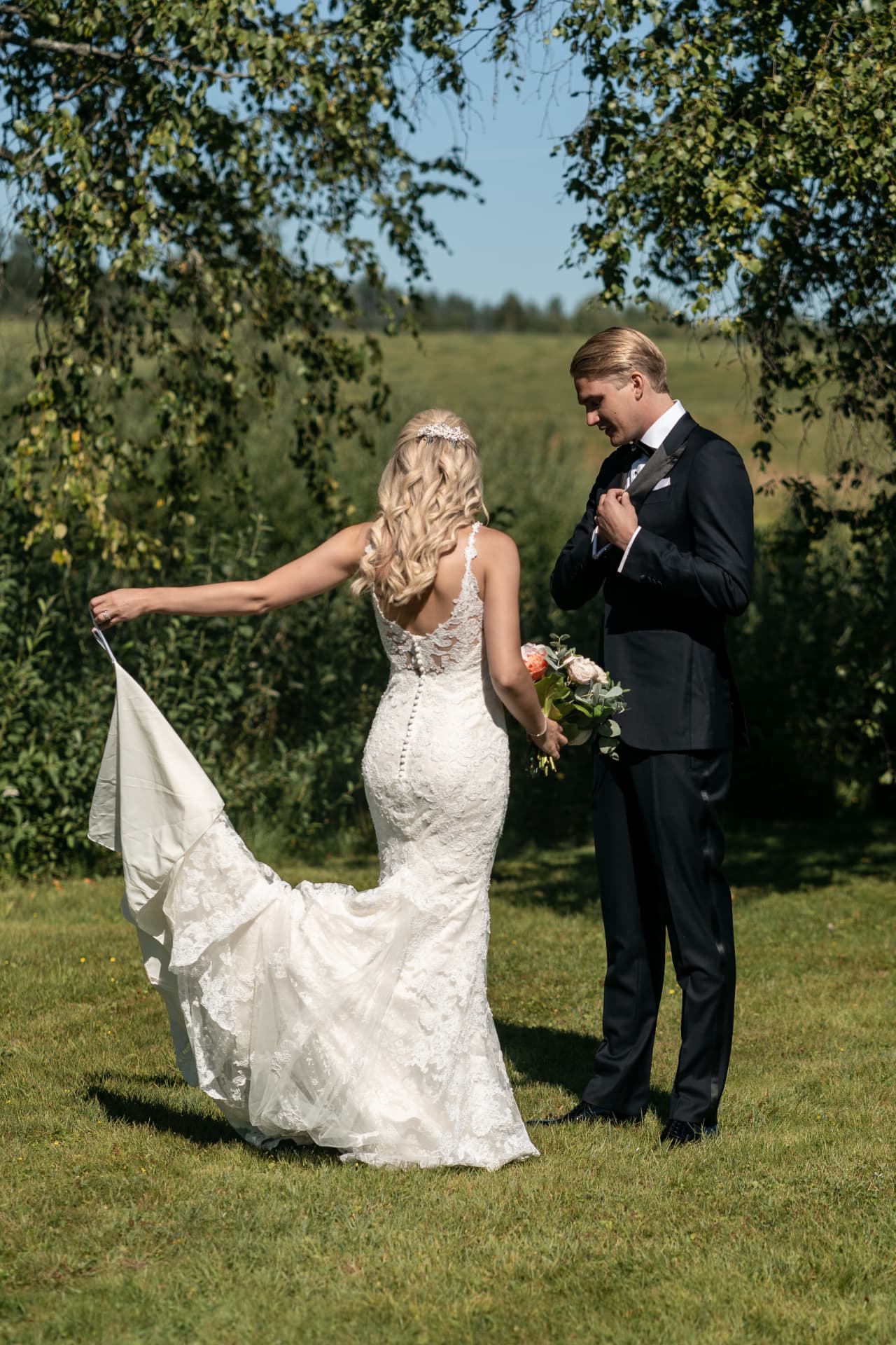 Bruden visar upp sitt släp för brudgummen på gräsmattan – bröllopsfoto av Mehmet Budak