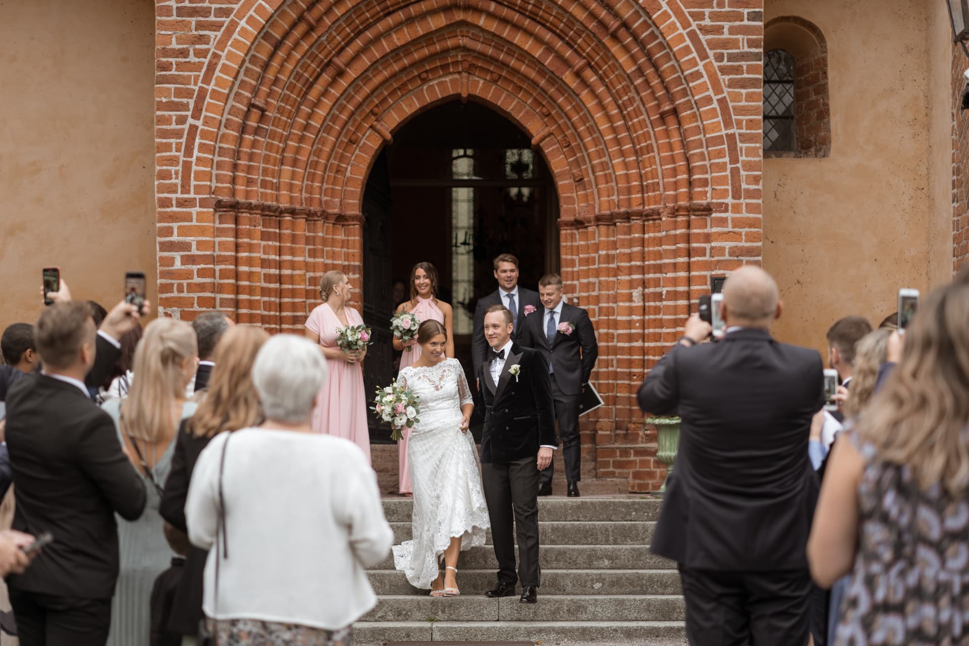 Brudparet går ut ur kyrkan följda av tärnor och marskalkar – bröllopsfoto av Mehmet Budak