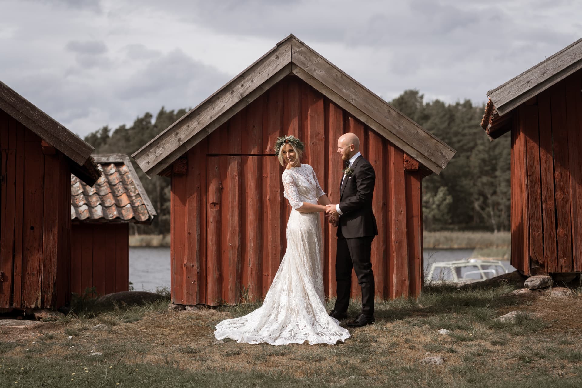 Brudparet framför gamla röda sjöbodar vid vattnet – bröllopsfoto av Mehmet Budak