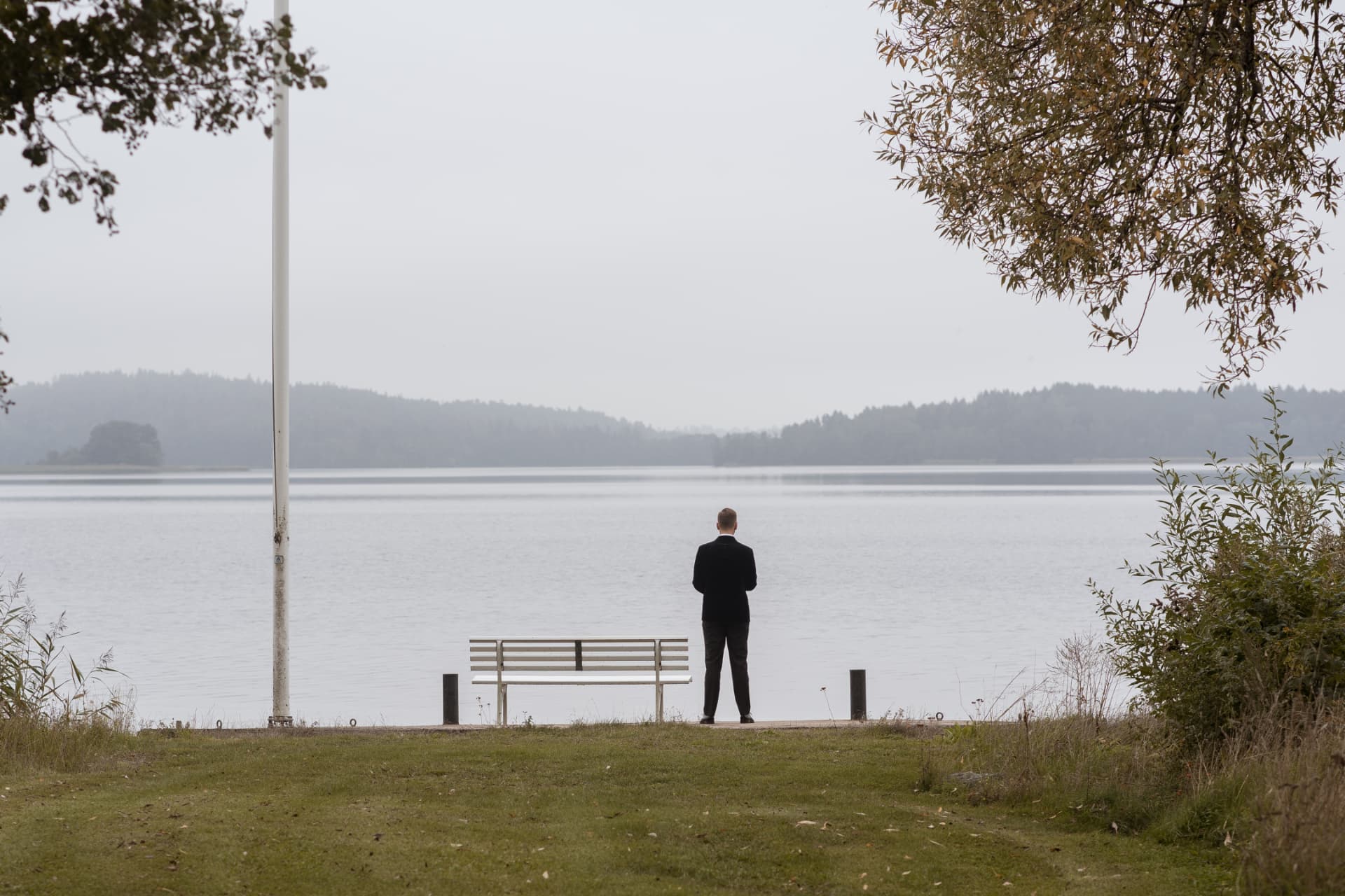 Brudgummen står ensam vid bänken och ser ut över Mälaren – bröllopsfoto av Mehmet Budak