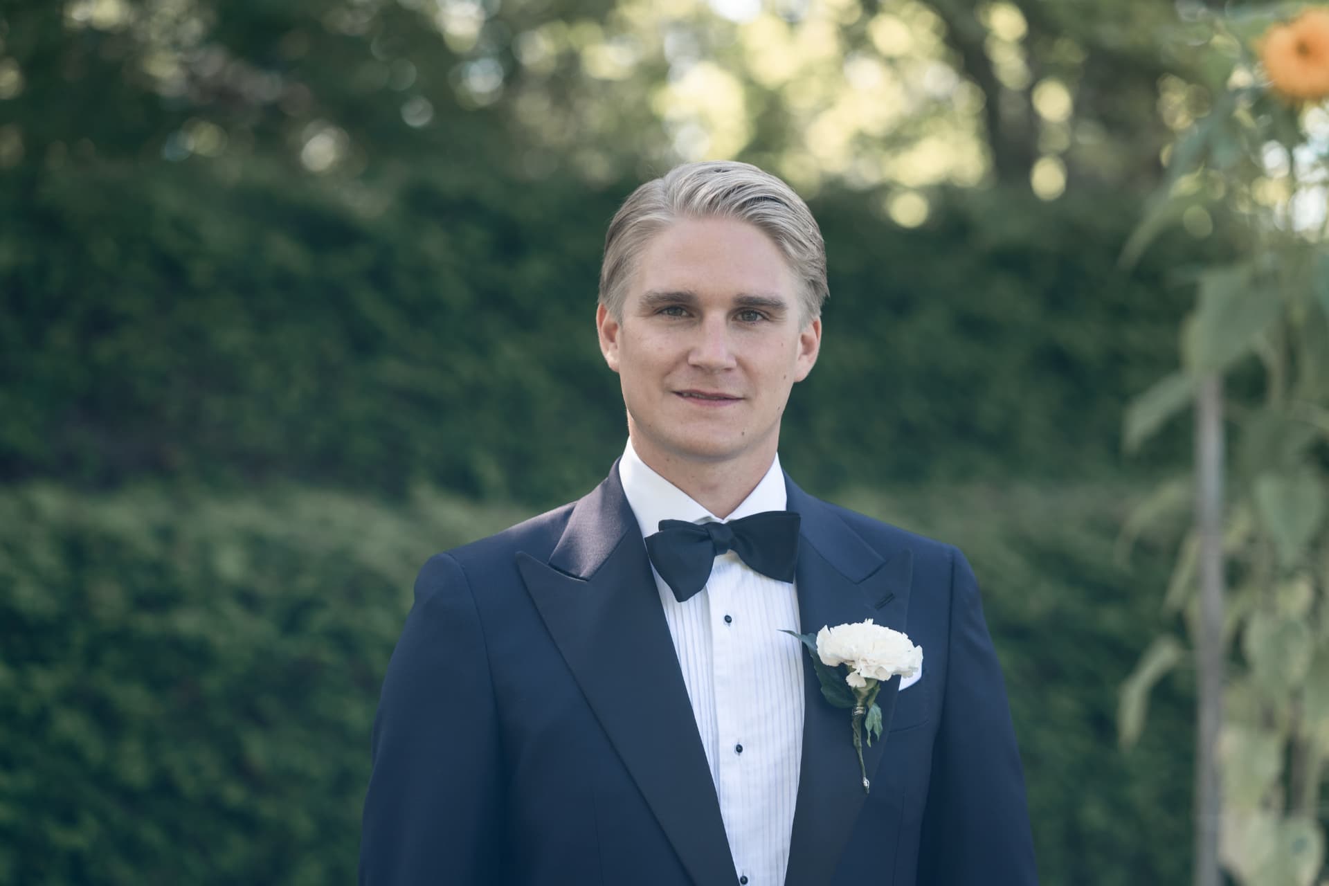 Porträtt av brudgummen i mörkblå smoking framför grönskan vid Ulvsunda Herrgård – bröllopsfoto av Mehmet Budak