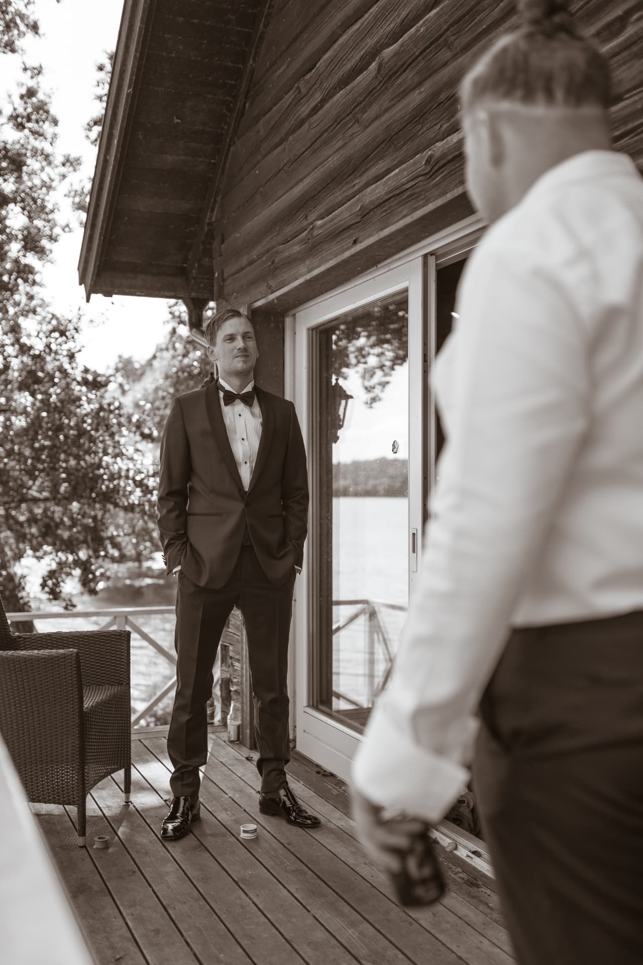 Brudgummen färdigklädd i smoking på verandan vid sjön, svartvitt – bröllopsfoto av Mehmet Budak