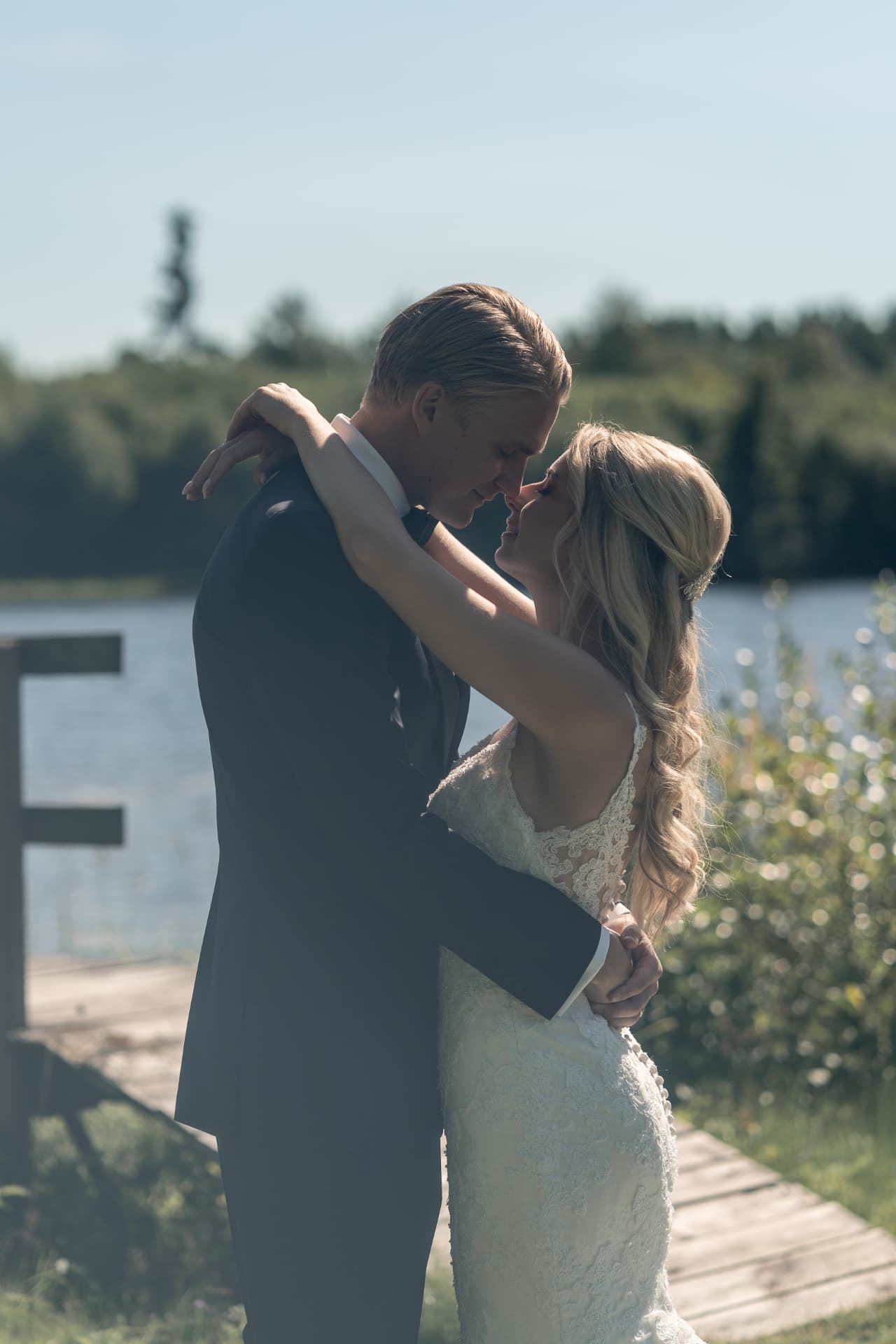 Brudparet står panna mot panna vid bryggan i sommarsolen – bröllopsfoto av Mehmet Budak