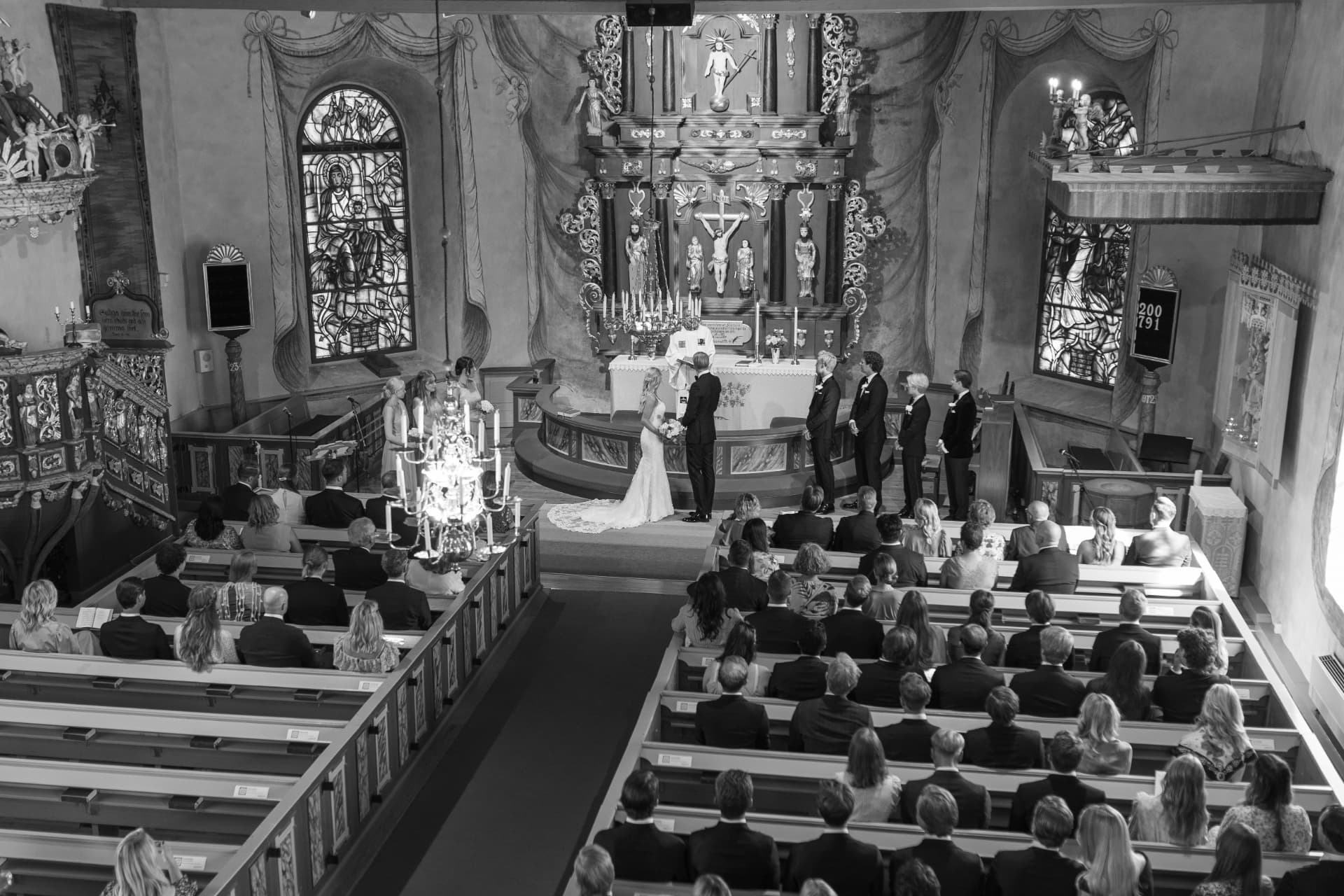 Vigseln sedd från läktaren med brudparet vid altaret och kyrkan full av gäster, svartvitt – bröllopsfoto av Mehmet Budak
