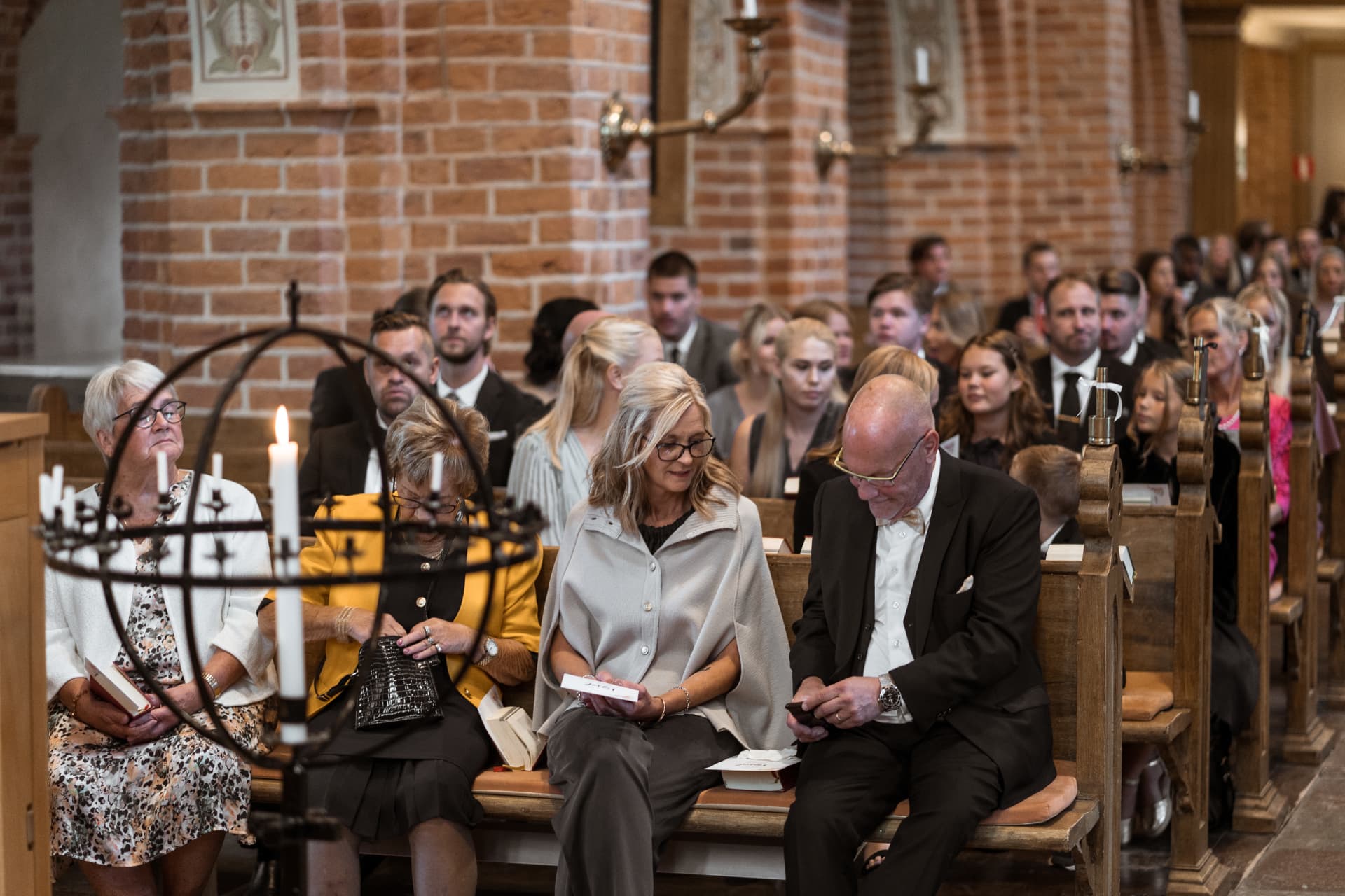 Familjen sitter i kyrkbänkarna med levande ljus framför – bröllopsfoto av Mehmet Budak