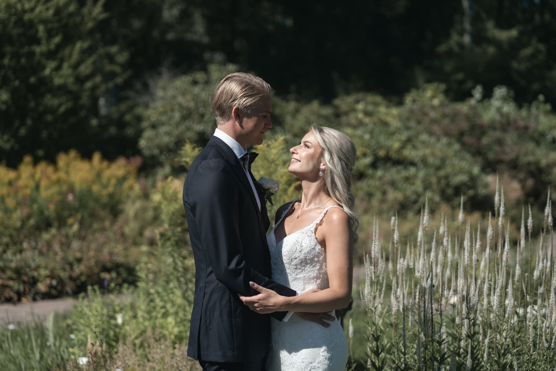 Brudparet ser varandra i ögonen bland blommorna i herrgårdsparken – bröllopsfoto av Mehmet Budak