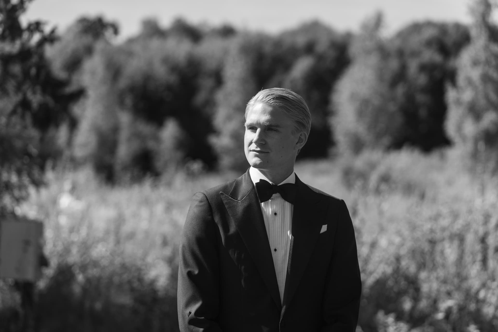 Porträtt av brudgummen i smoking framför ängen, svartvitt – bröllopsfoto av Mehmet Budak