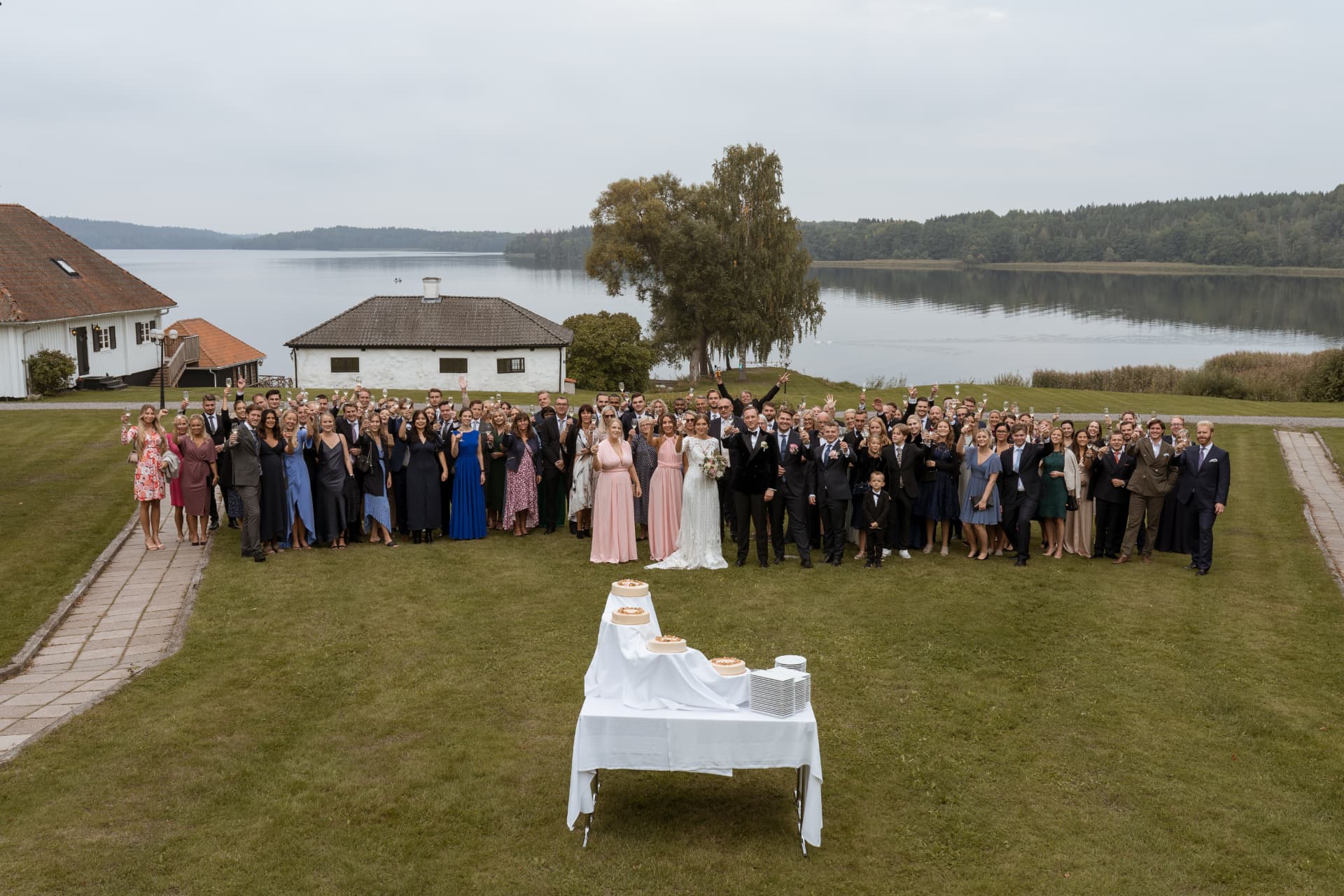 Brudparet och alla gäster samlade på gräsmattan vid Mälaren – bröllopsfoto av Mehmet Budak