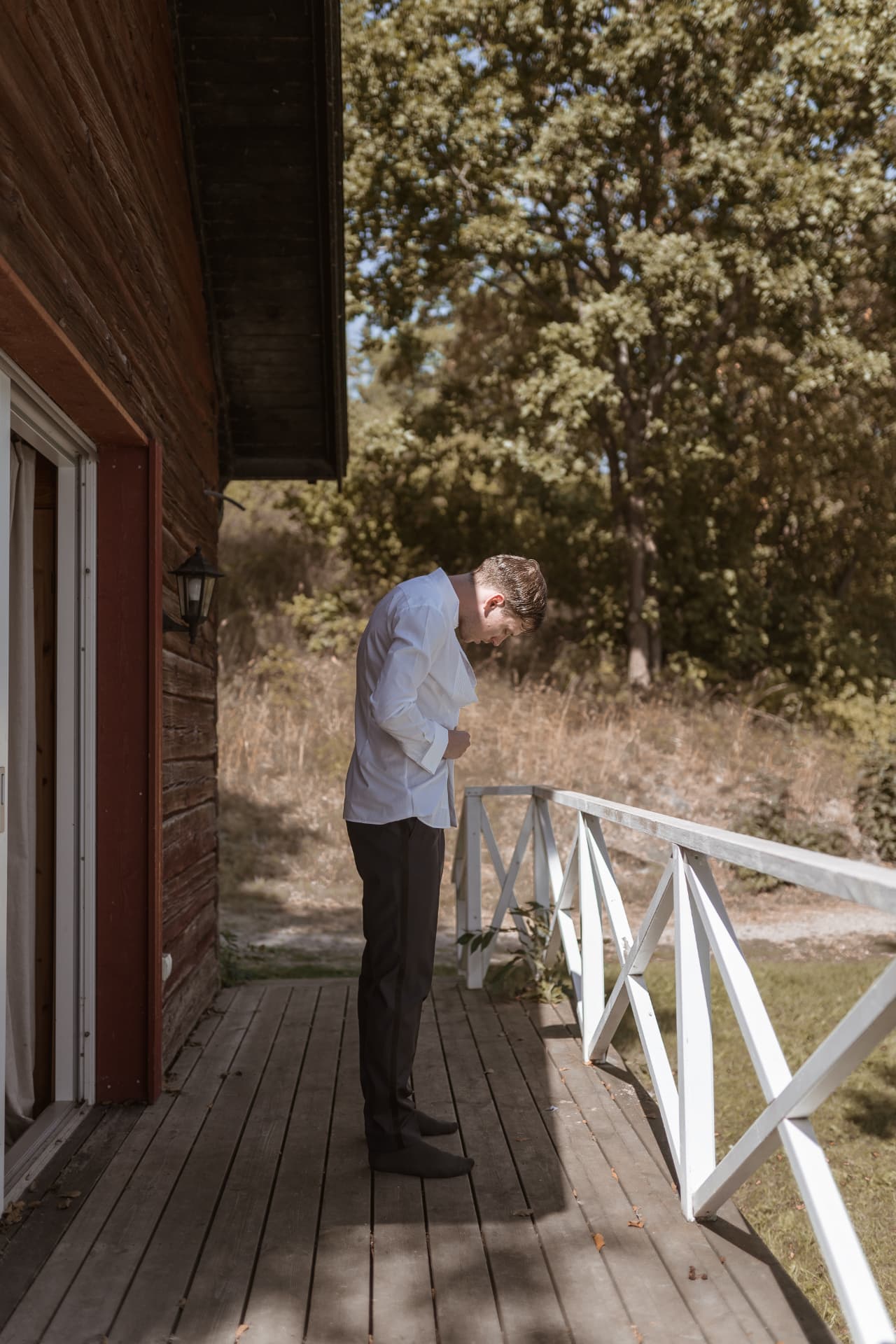 Brudgummen knäpper skjortan på stugans veranda – bröllopsfoto av Mehmet Budak
