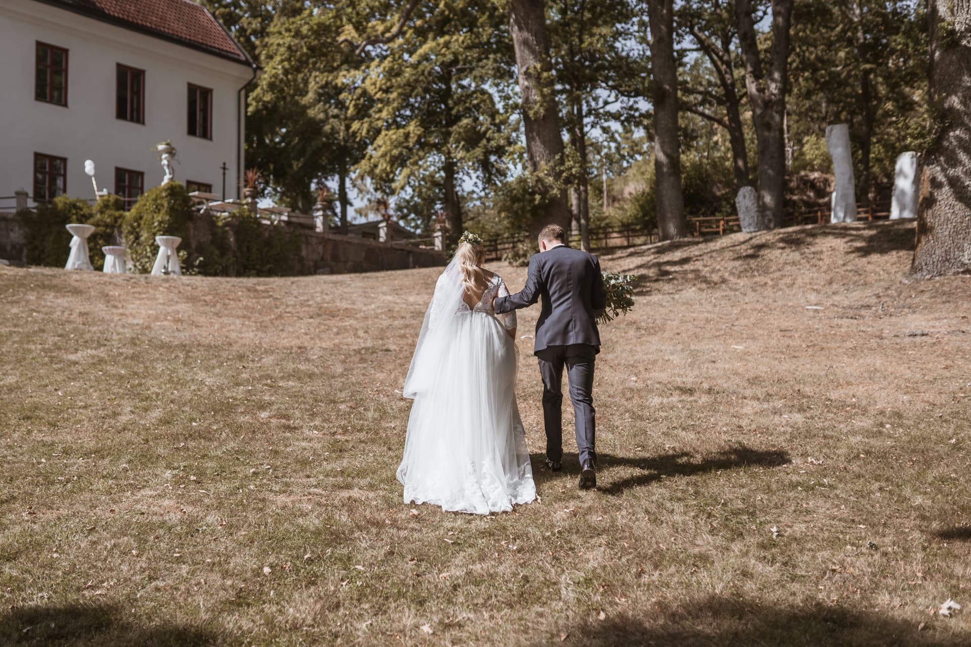 Brudparet går hand i hand upp mot Ulvhälls Herrgård – bröllopsfoto av Mehmet Budak