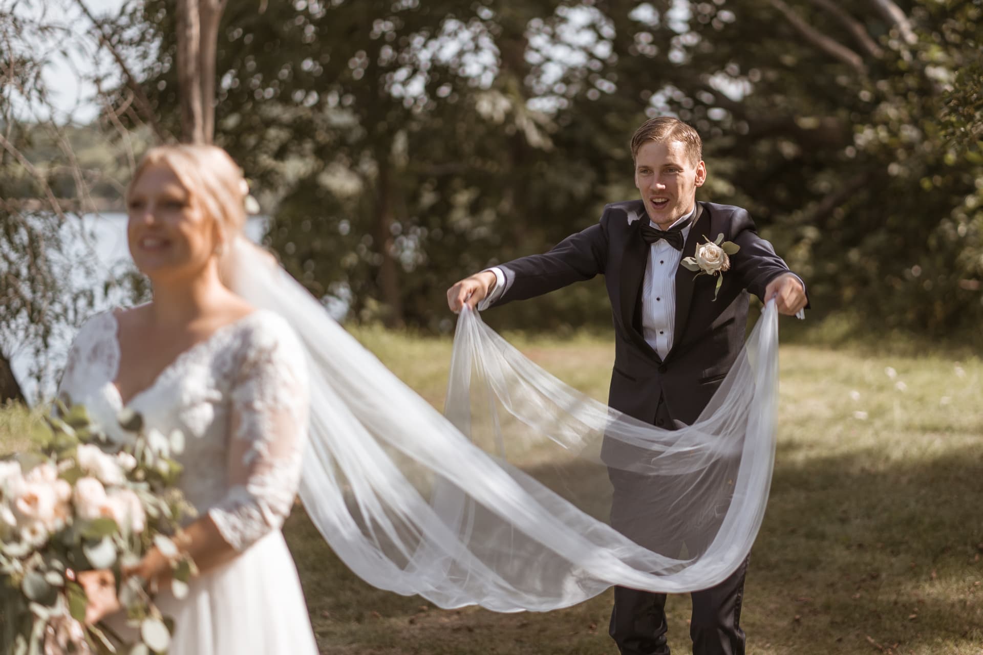 Brudgummen håller ut brudens slöja bakom henne i solen – bröllopsfoto av Mehmet Budak