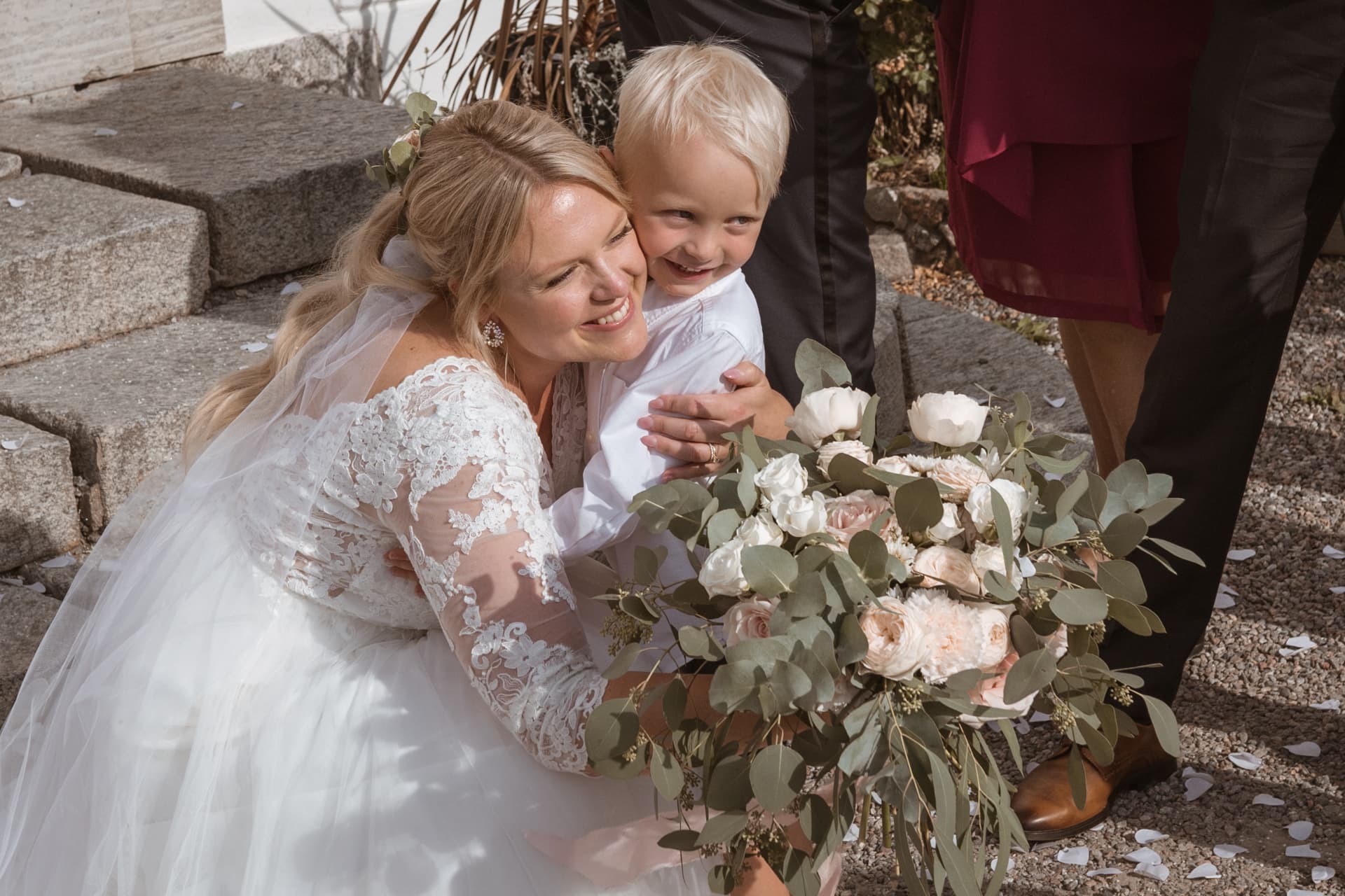 Bruden kramar en liten pojke på trappan med brudbuketten – bröllopsfoto av Mehmet Budak
