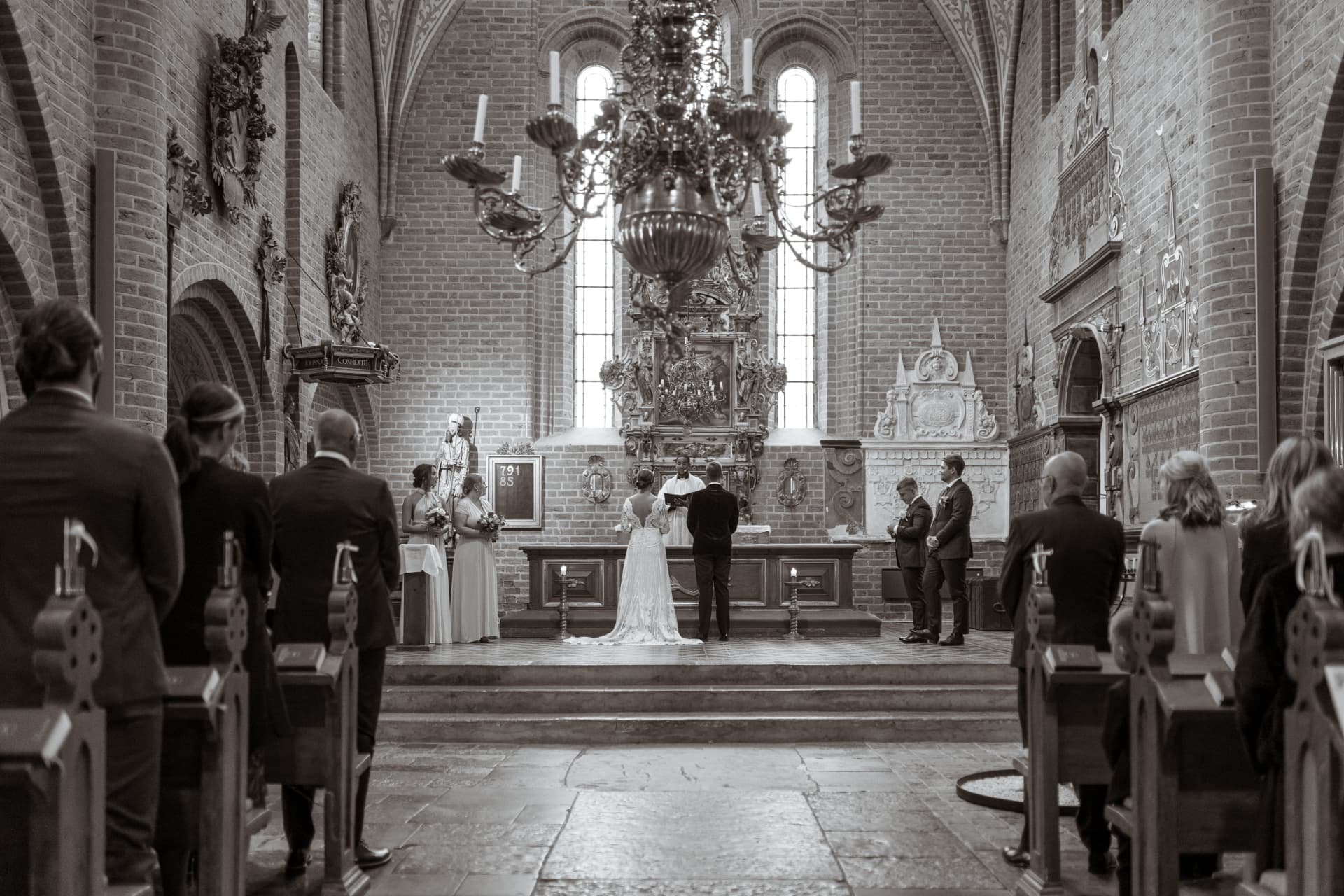 Vigseln sedd genom kyrkan med gästerna stående, sepiaton – bröllopsfoto av Mehmet Budak