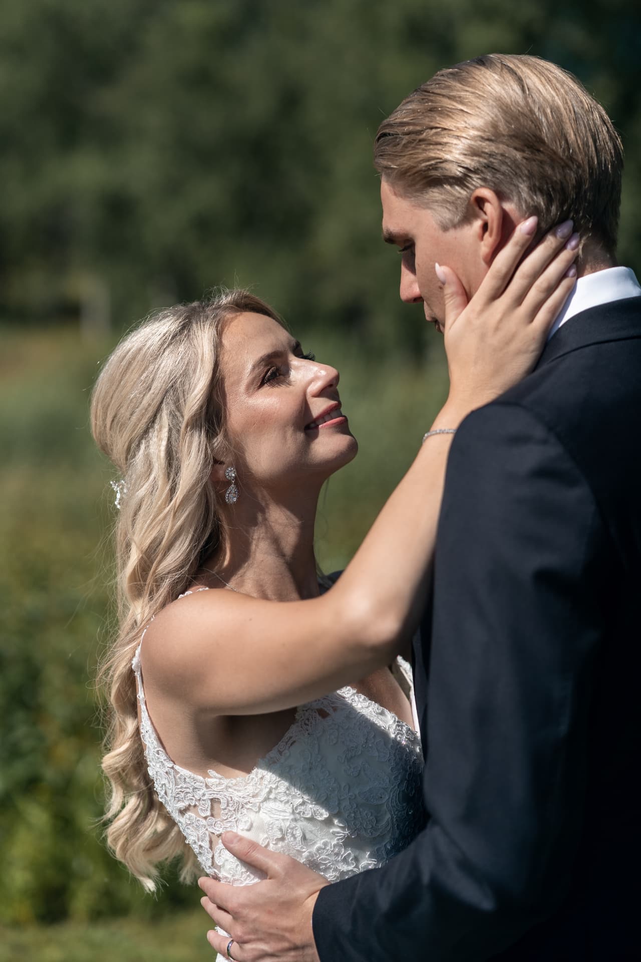 Bruden håller om brudgummens ansikte i solljuset vid Ulvsunda Herrgård – bröllopsfoto av Mehmet Budak