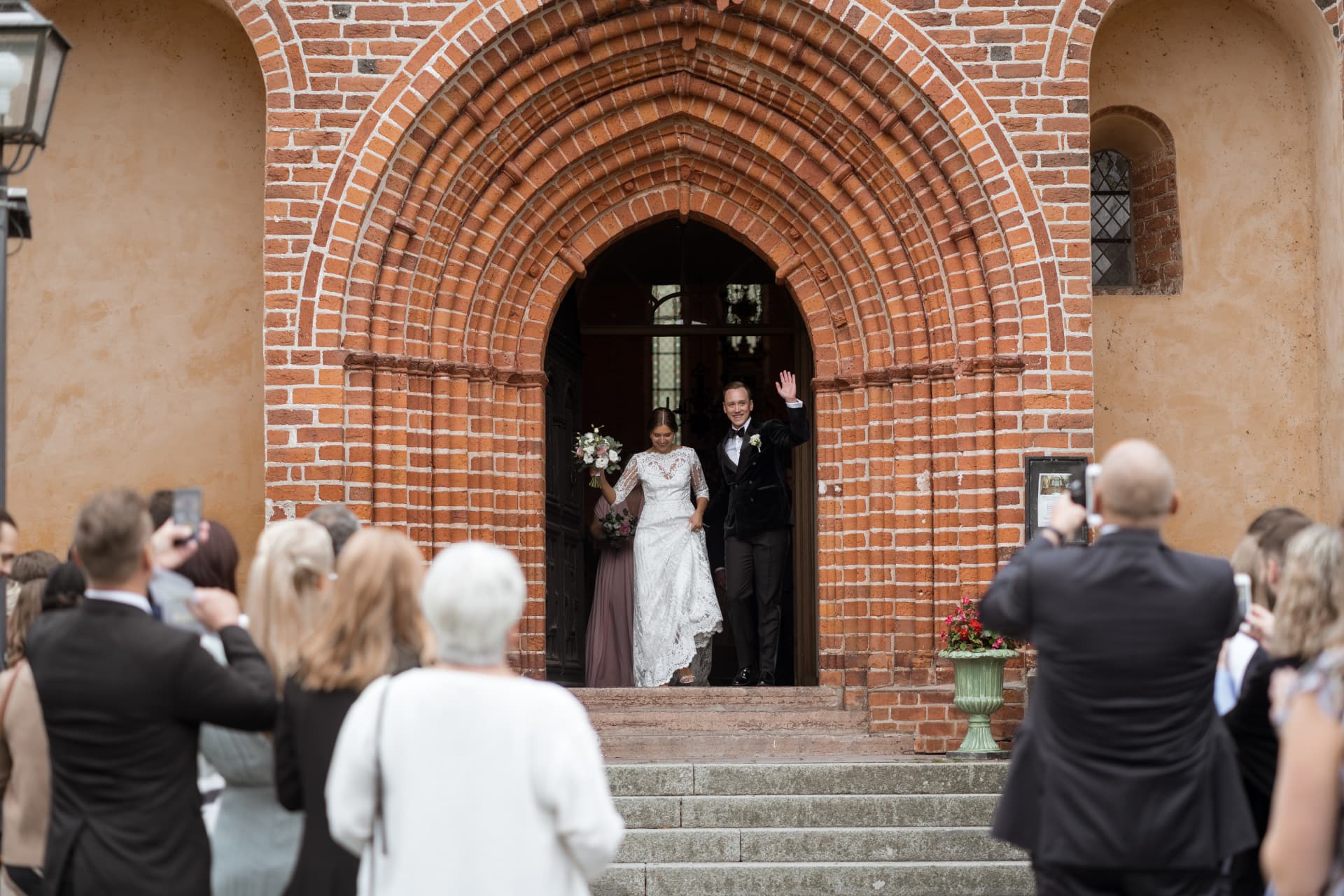 Brudparet vinkar i kyrkportalen efter vigseln – bröllopsfoto av Mehmet Budak