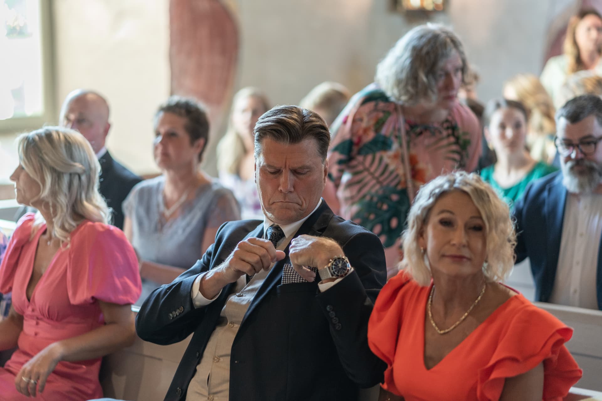 En gäst rättar till bröstfickan i kyrkbänken bland de övriga gästerna – bröllopsfoto av Mehmet Budak