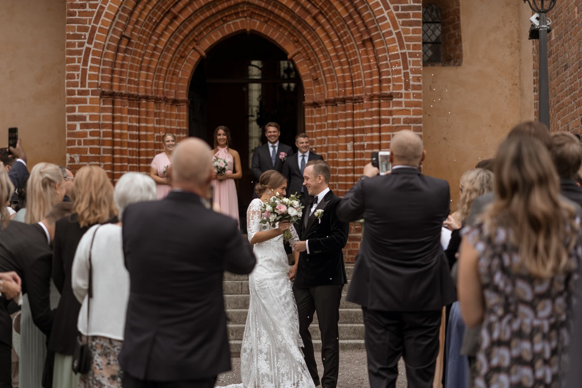 Brudparet skrattar tillsammans bland gästerna utanför kyrkan – bröllopsfoto av Mehmet Budak