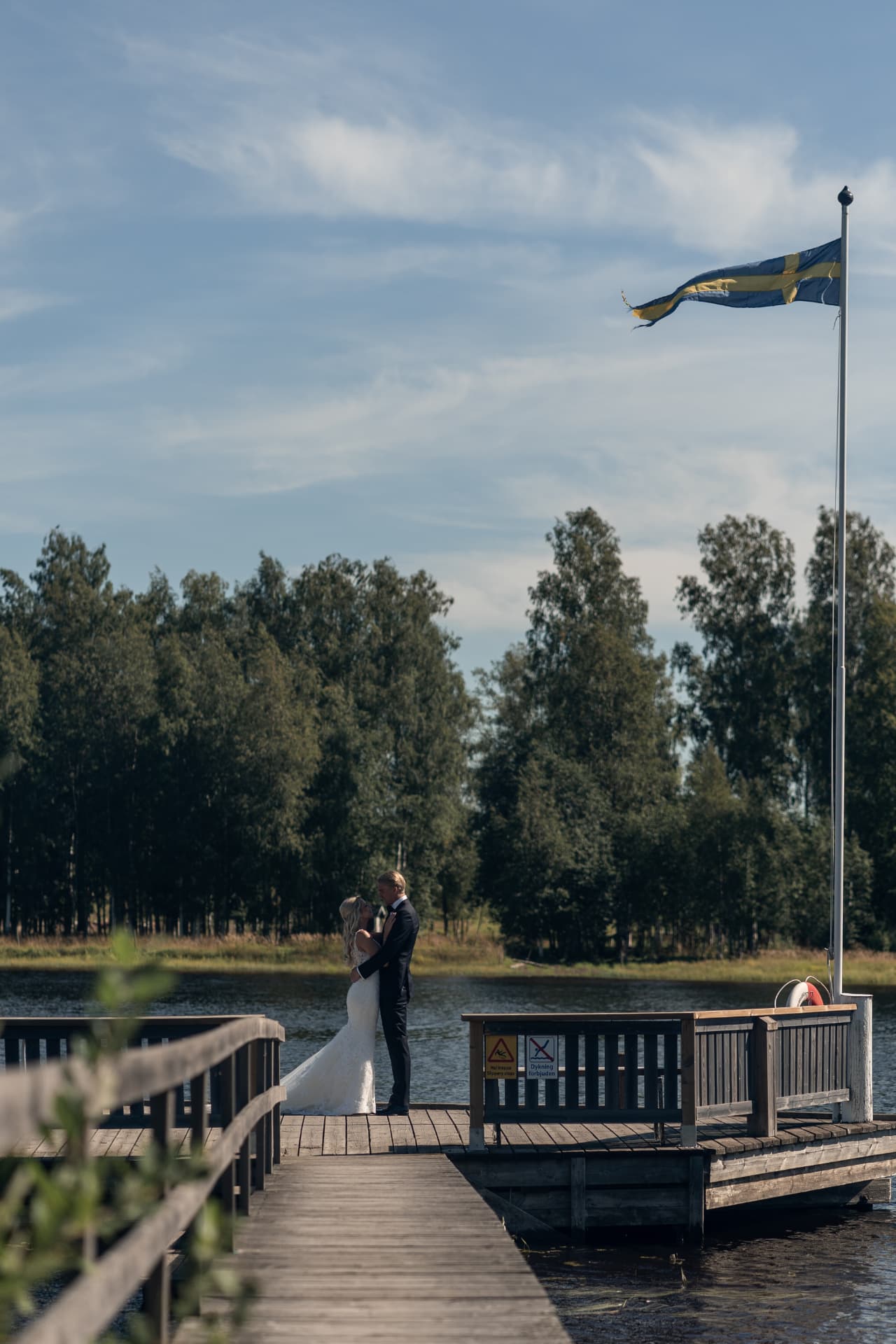 Brudparet omfamnar varandra längst ut på bryggan under flaggstången – bröllopsfoto av Mehmet Budak